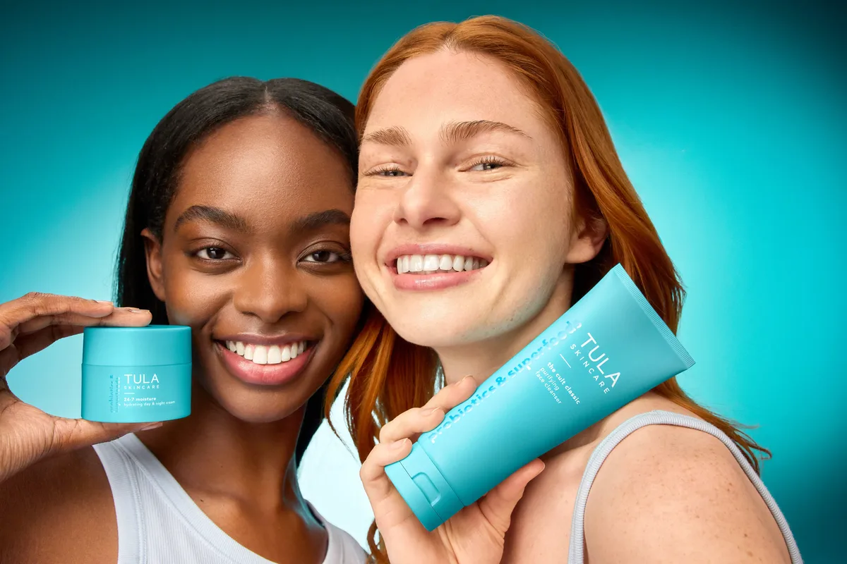 Two smiling women holding TULA cleanser and moisturizer
