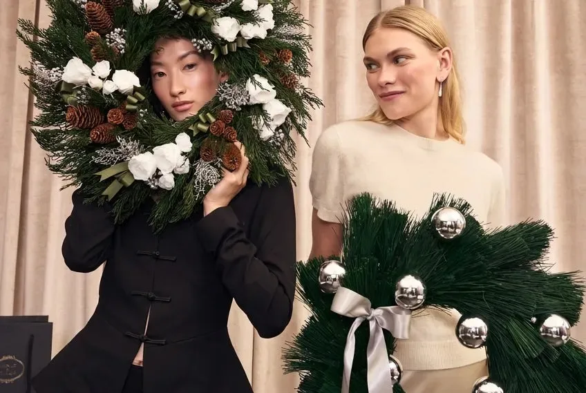 Two women holding Venus et Fleur® holiday wreaths against softly draped curtains