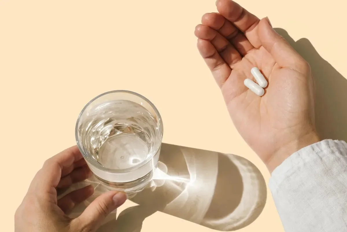 Two capsules held beside a glass of water